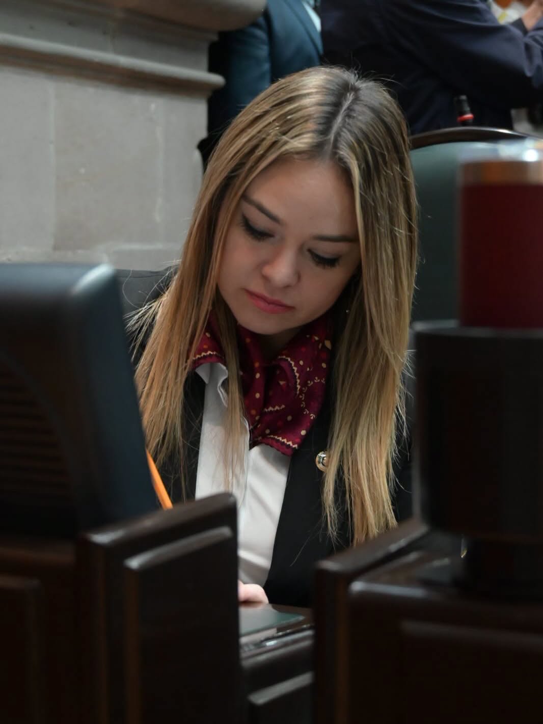 Mujer con gafas revisa gráficos en portapapeles en un escritorio.